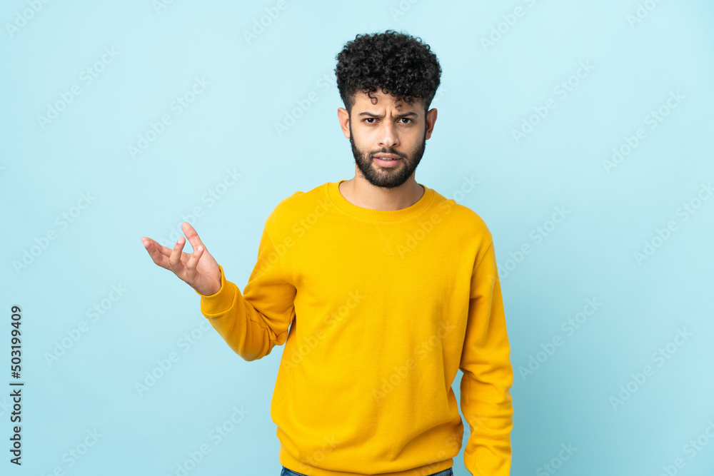 Young Moroccan man isolated on blue background making doubts gesture Young Moroccan man isolated on blue background making doubts gesture