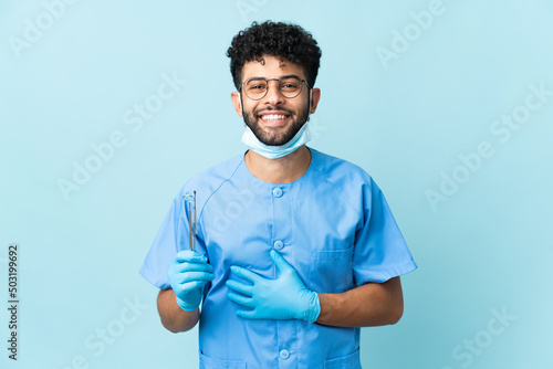 Moroccan dentist man holding tools isolated on blue background smiling a lot