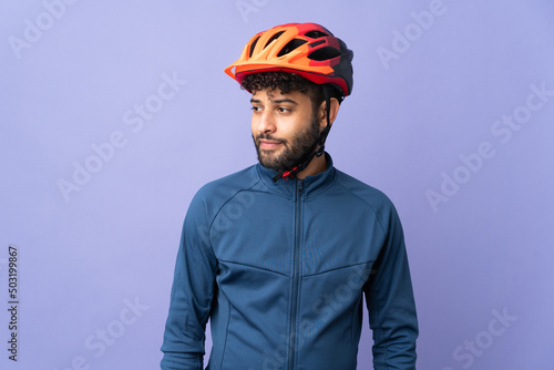 Young Moroccan cyclist man isolated on purple background looking to the side and smiling © luismolinero