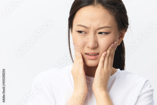 Gumboil Dental abscess Wisdom teeth Periodontitis. Unhappy suffering tanned pretty young Asian woman touch cheek posing isolated on white background. Injuries Poor health Illness concept. Cool offer © SHOTPRIME STUDIO