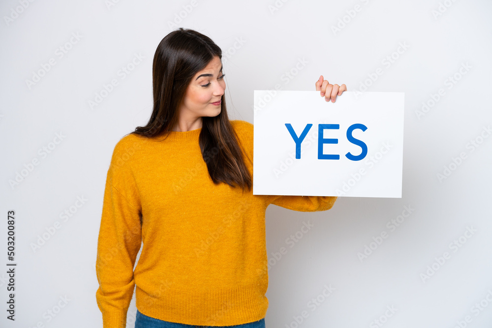Young Brazilian woman isolated on white background holding a placard with text YES Young Brazilian woman isolated on white background holding a placard with text YES