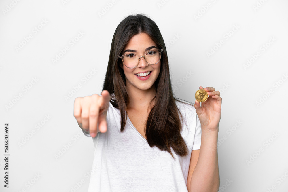 Young Brazilian woman holding a Bitcoin isolated on white background points finger at you with a confident expression Young Brazilian woman holding a Bitcoin isolated on white background points finger at you with a confident expression