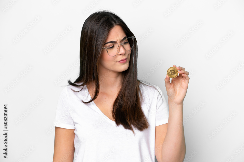 Young Brazilian woman holding a Bitcoin isolated on white background with sad expression Young Brazilian woman holding a Bitcoin isolated on white background with sad expression
