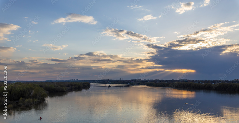 Evening landscape, sunset on the river. Wide river, horizon, clouds are reflected in the water. Sunlight through the clouds.