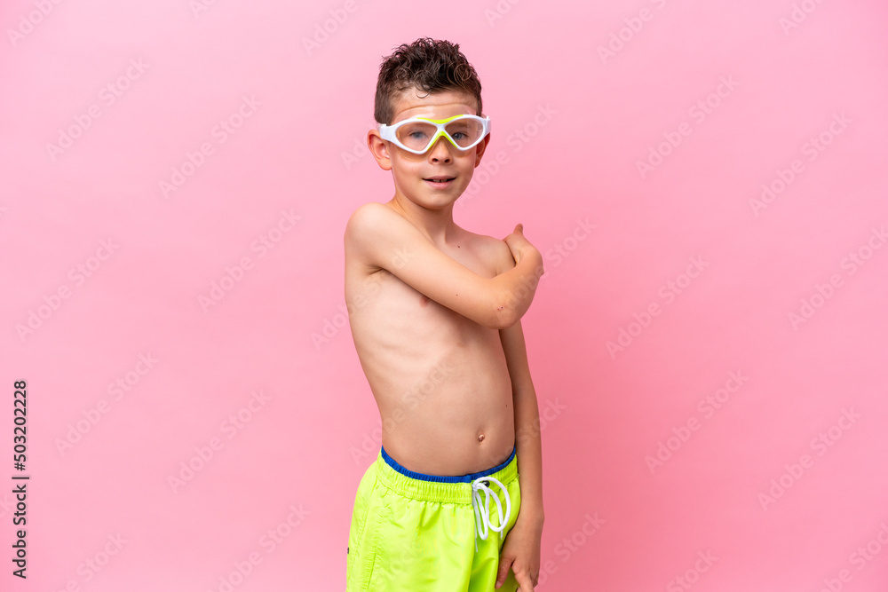 Little caucasian boy wearing a diving goggles isolated on pink background pointing back