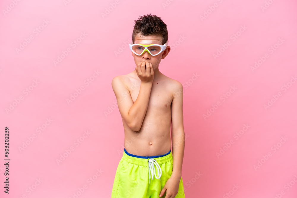 Little caucasian boy wearing a diving goggles isolated on pink background having doubts