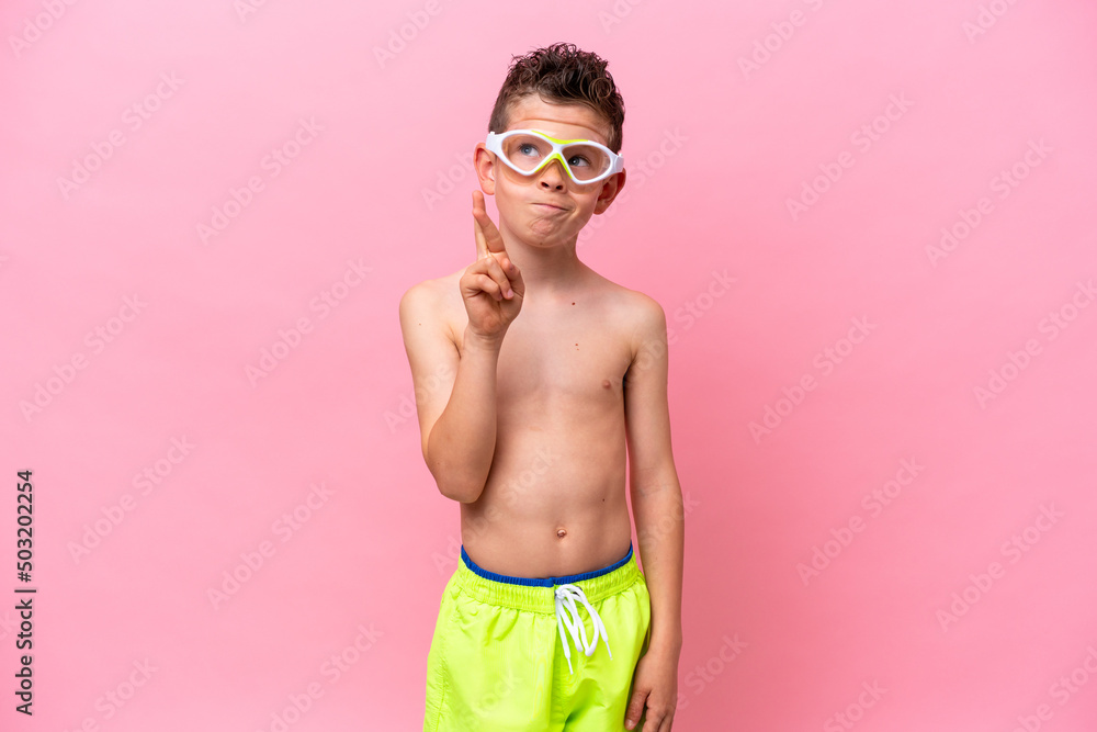 Little caucasian boy wearing a diving goggles isolated on pink background with fingers crossing and wishing the best Little caucasian boy wearing a diving goggles isolated on pink background with fingers crossing and wishing the best