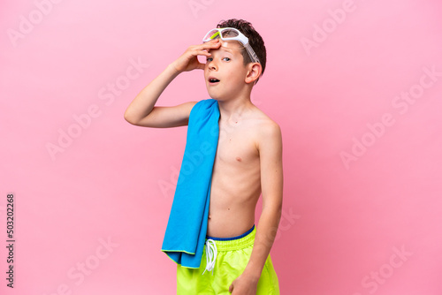 Little caucasian boy wearing a diving goggles isolated on pink background doing surprise gesture while looking to the side