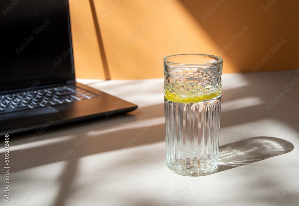 A glass of water with lemon and a laptop on a beige background with beautiful sunny shadows. Digital detox concept, work break, water balance, healthy lifestyle A glass of water with lemon and a laptop on a beige background with beautiful sunny shadows. Digital detox concept, work break, water balance, healthy lifestyle