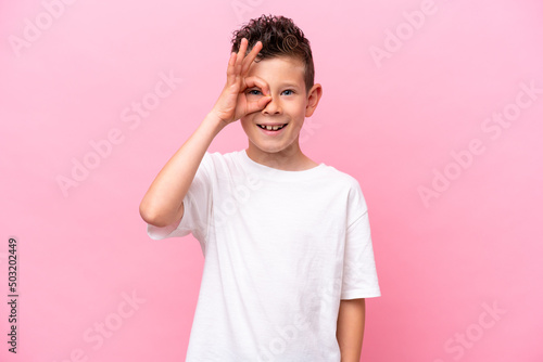 Little caucasian boy isolated on pink background showing ok sign with fingers