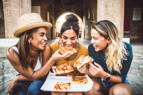 Three young female friends eating pizza sitting outside - Happy women enjoying street food in the city - Italian food culture and european holidays concept