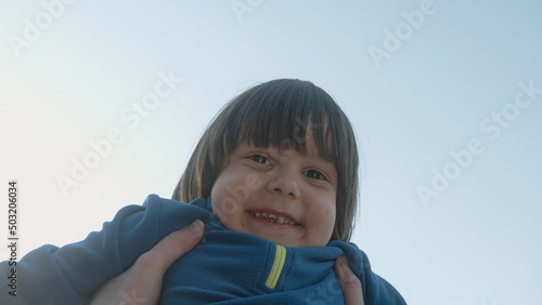 Cute dressed up smiling smiling child or baby is being lifted into the air by his father and they are enjoying this beautiful summer day together by playing cheerfully