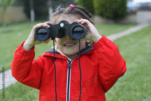 Four years old girl close up, looking through binoculars.