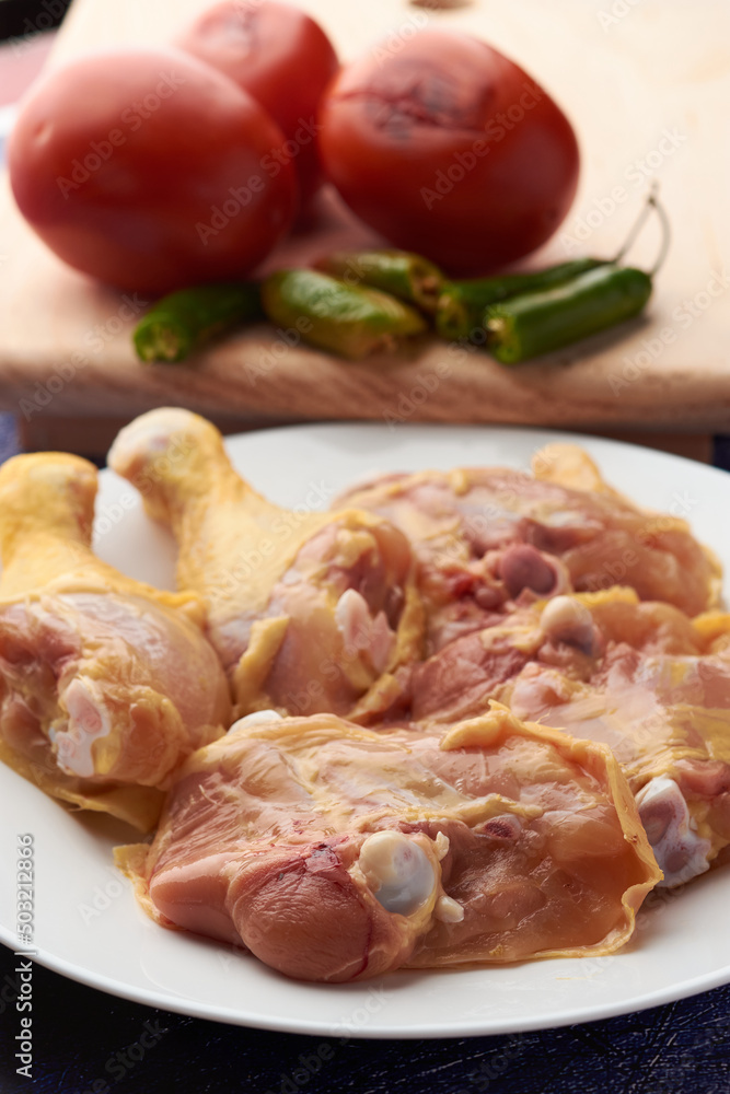 Chicken pieces placed on a plate, garnish tomatoes and chili peppers placed on a wood.