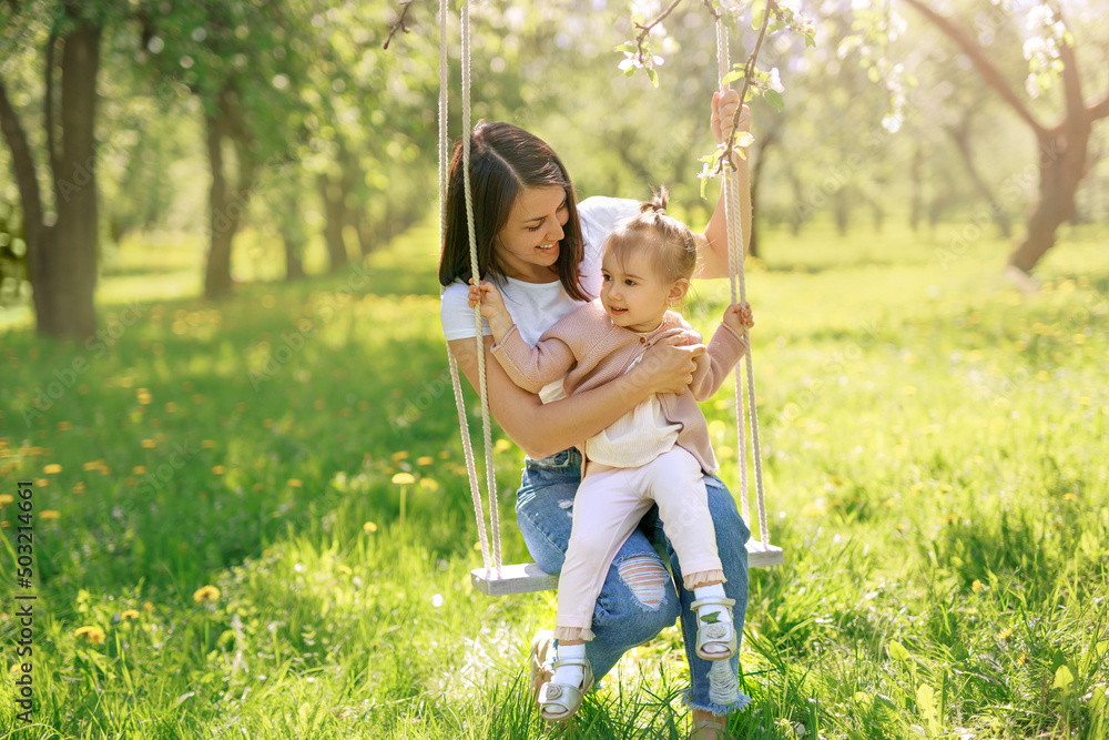 Mom and daughter swinging  on a swing in a blooming garden on a hot spring day. The child has fun with his mother. Mother's day