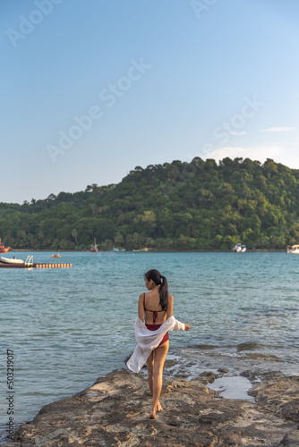 Female tourist wear swimming suit and stand alone at rock on the beach