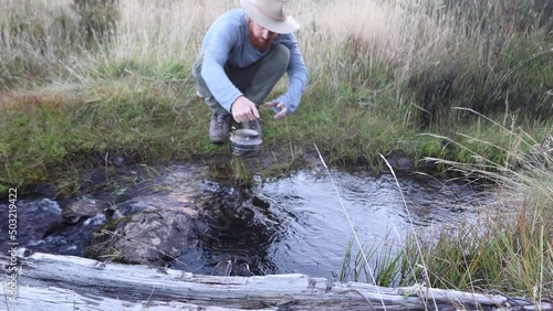 A bushman with an akubra hat fills up his billy in a high country creek. photo