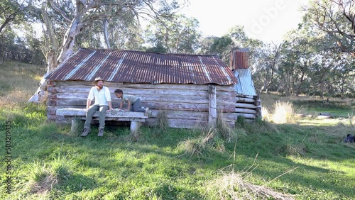 A man and son sit next to an old wooden hut up in alpine country Australia. photo