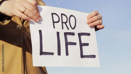 Female holding PRO LIFE board against blue sky, close up view photo