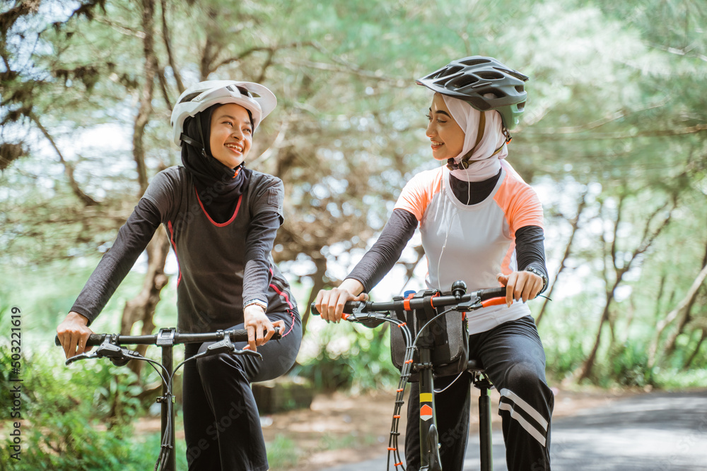 Obraz premium Two Muslim women in sportswear and cycling helmets on outdoor background