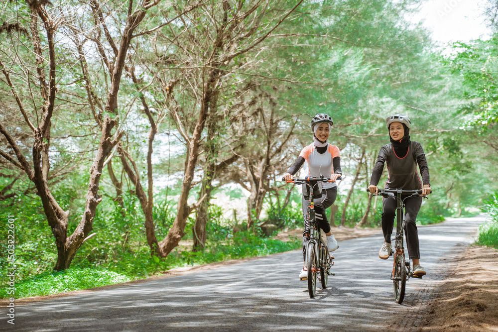 two asian muslim women cycling on the road many trees background