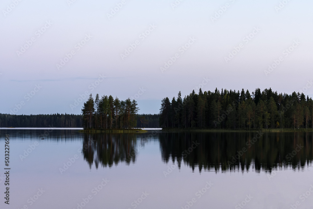 Calm lake in the summer evening in Finland with islands and trees reflecting from the water.