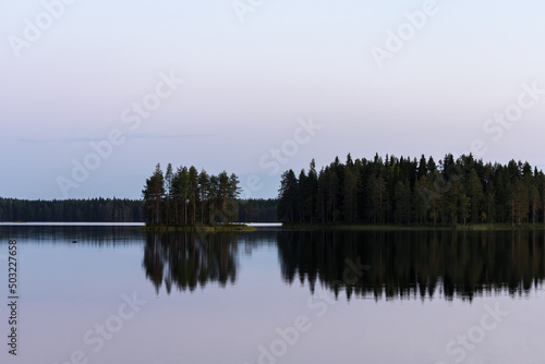 Calm lake in the summer evening in Finland with islands and trees reflecting from the water.