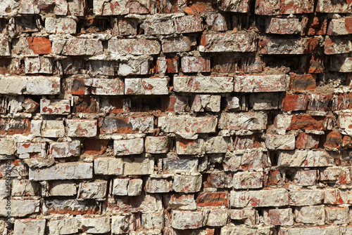 Old brick wall texture. The wall, made of old red bricks, darkened by old age. Ancient vintage brick wall background. Brick wall backdrop. Crumbling and chipped brickwork with traces of whitewash