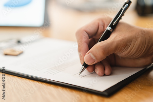 close up hand of person signing signature to contract document on the table with bank