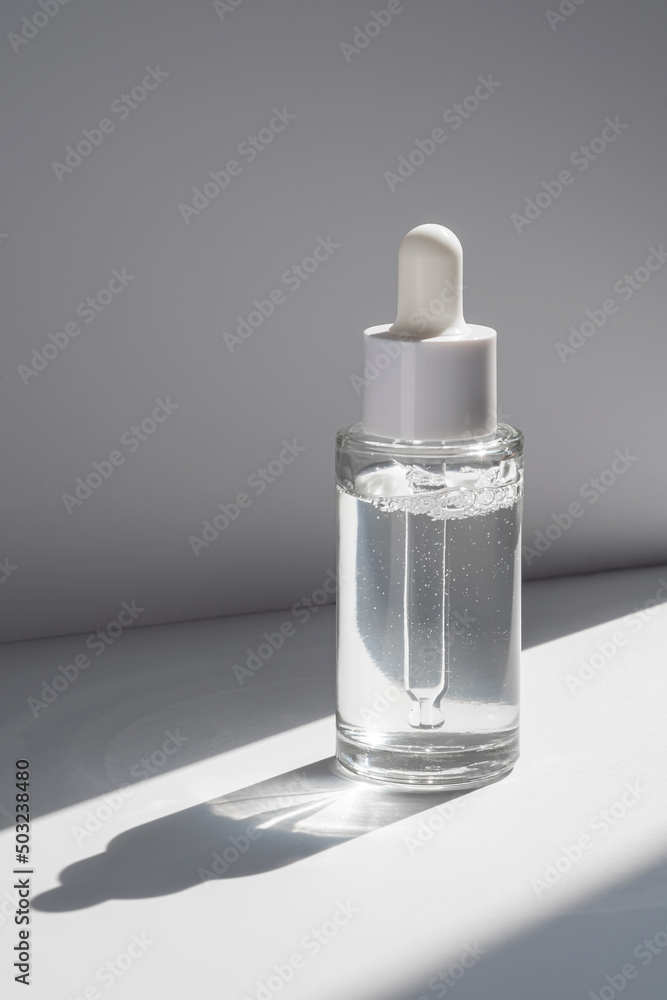 A white transparent bottle with serum in the rays of the sun. A white transparent bottle with serum in the rays of the sun.