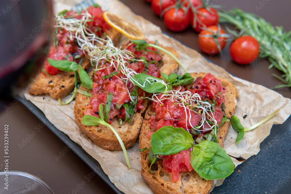 a bruschetta with tomatoes on a dark table, a glass of red wine a bruschetta with tomatoes on a dark table, a glass of red wine