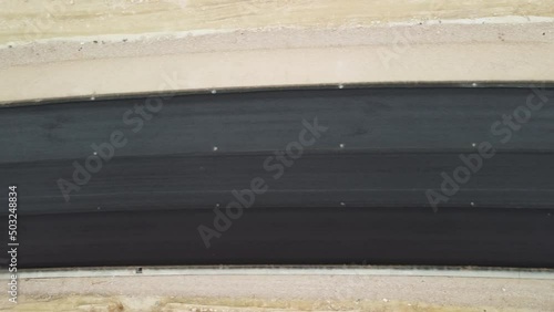 yellow truck pouring bitumen over a new road. Aerial drone shot. Road construction in progress on slope nature canyon. Infrastructure development and logistics.