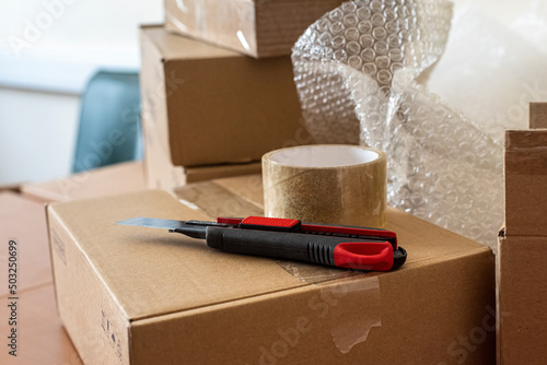 фотографія construction knife and sticky transparent tape on the packing box on the desk in