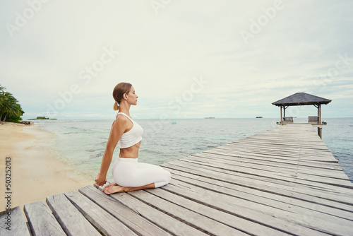 Yoga on the beach. Young woman stretching on wooden pier with sea view. © luengo_ua