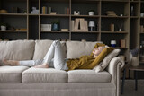 Peaceful calm mature woman lying on sofa with closed eyes, sleeping, stretching body, enjoying break, silent leisure time at home, taking deep breath of fresh air, relaxing, reducing stress
