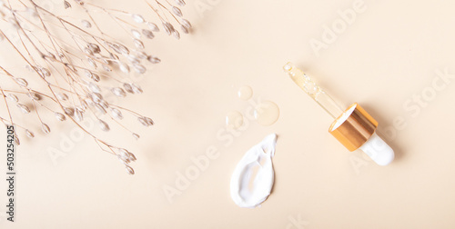 Cosmetic smear with cream and drops of oil, serum on a beige background top view banner format