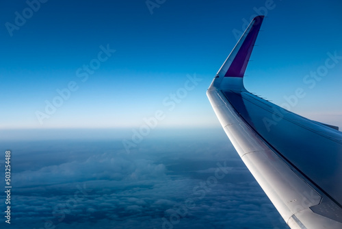  Wing of an airplane above the clouds. The view from the airplane window to the clouds and sunset. Airplane wing above thick white clouds. Wonderful breathtaking view.