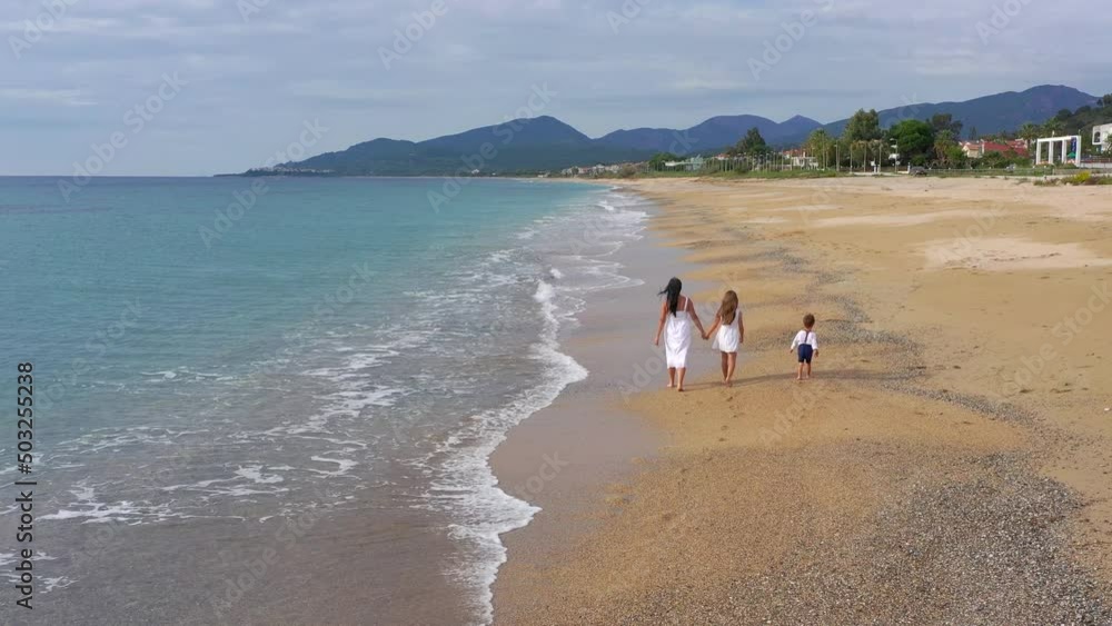 Happy mom with her beloved children hold hands and walk along the beach on summer vacation. Family, vacation and travel concept. Happy mom with her beloved children hold hands and walk along the beach on summer vacation. Family, vacation and travel concept.