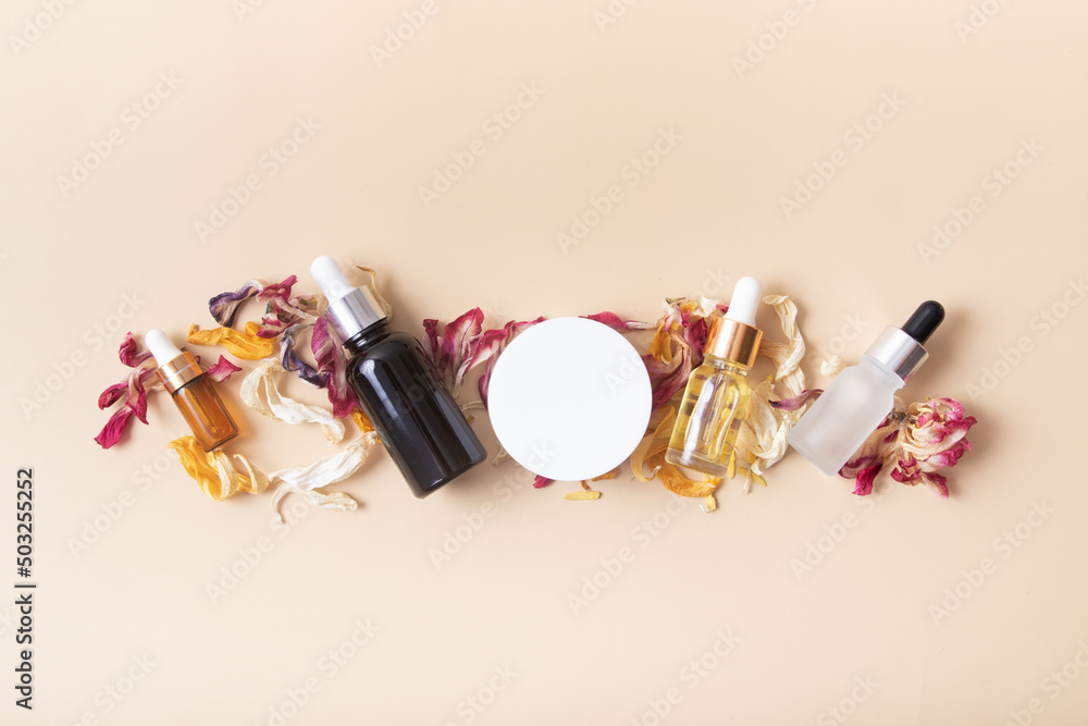 Cosmetic bottles and jar with dry colored flower petals on a beige background top view Cosmetic bottles and jar with dry colored flower petals on a beige background top view