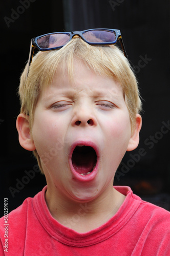 portait of a young boy yawning with glasses on his head   concept of tired or sleepy children .