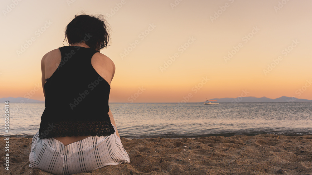 Unhappy single woman sitting on sand at sunset. Lonely young woman missing someone concept idea. Time to go, say goodbye or good bye. Empty copy space for advertising banners and ad texts.