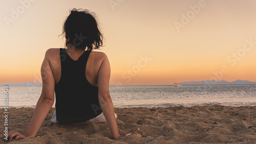 Alone single woman sitting on sand at sunset, looking at distant sea or seascape horizon. Missing someone concept idea. Time to go, say goodbye or good bye. Copy space for advertising banners, ad text
