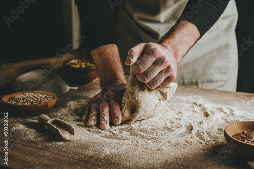 Fototapeta Young man kneading dough on dark background.