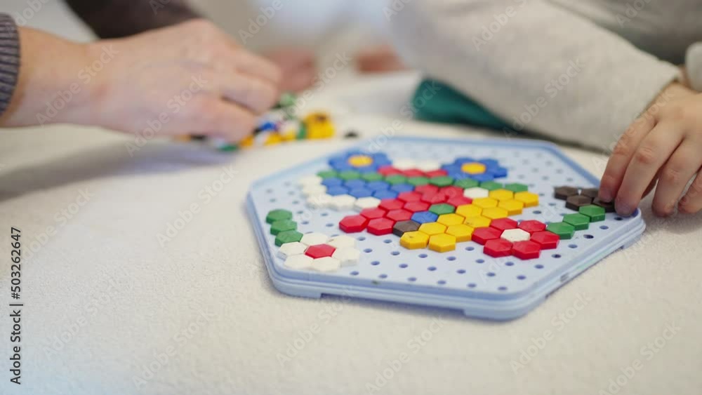 the hands of an adult woman help a child to assemble a mosaic. educational games for children the hands of an adult woman help a child to assemble a mosaic. educational games for children