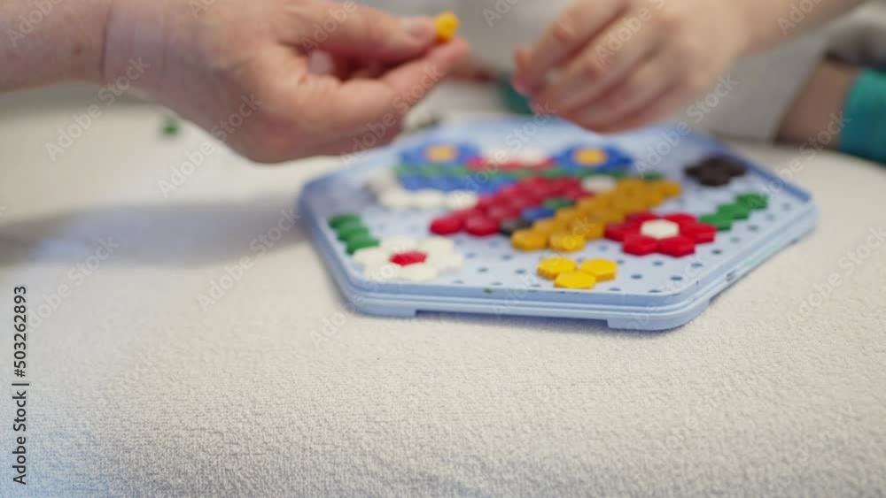 children's hands collect a colored mosaic on a stand, an adult helps children's hands collect a colored mosaic on a stand, an adult helps