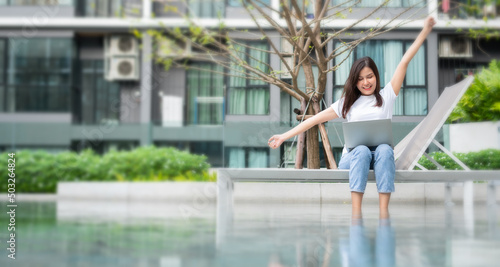 Happy young entrepreneur woman sitting on tanning bed beside pool and using laptop computer for remote online working digital, online business project in quiet yard of resort house, Work on vacation