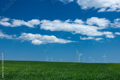 Wind turbine on a green field with blue sky and clouds