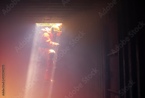 A firefighter in suit and helmet is climbing down the stair with fire to helping the victim.