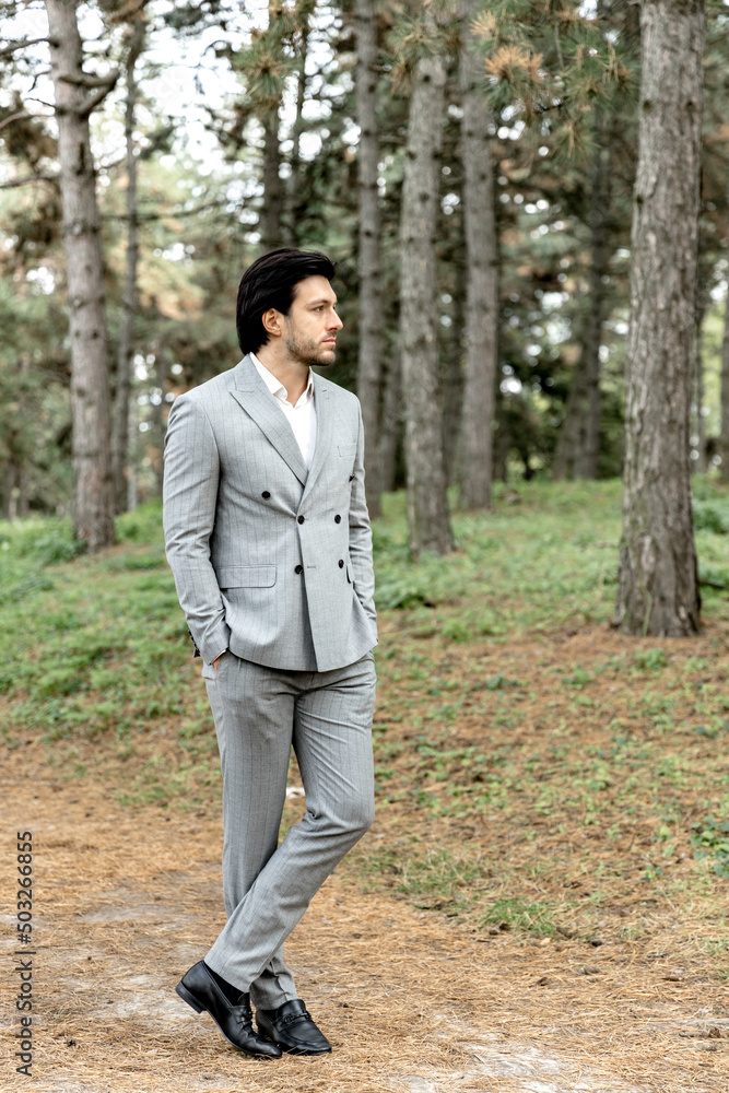 A handsome successful man in a gray suit stands against the background of the forest