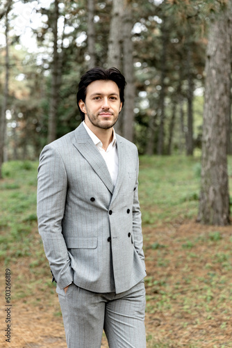 A handsome successful man in a gray suit stands against the background of the forest